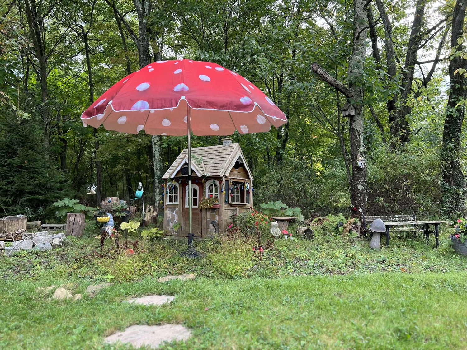 Red toadstool umbrella over a whimsical garden playhouse